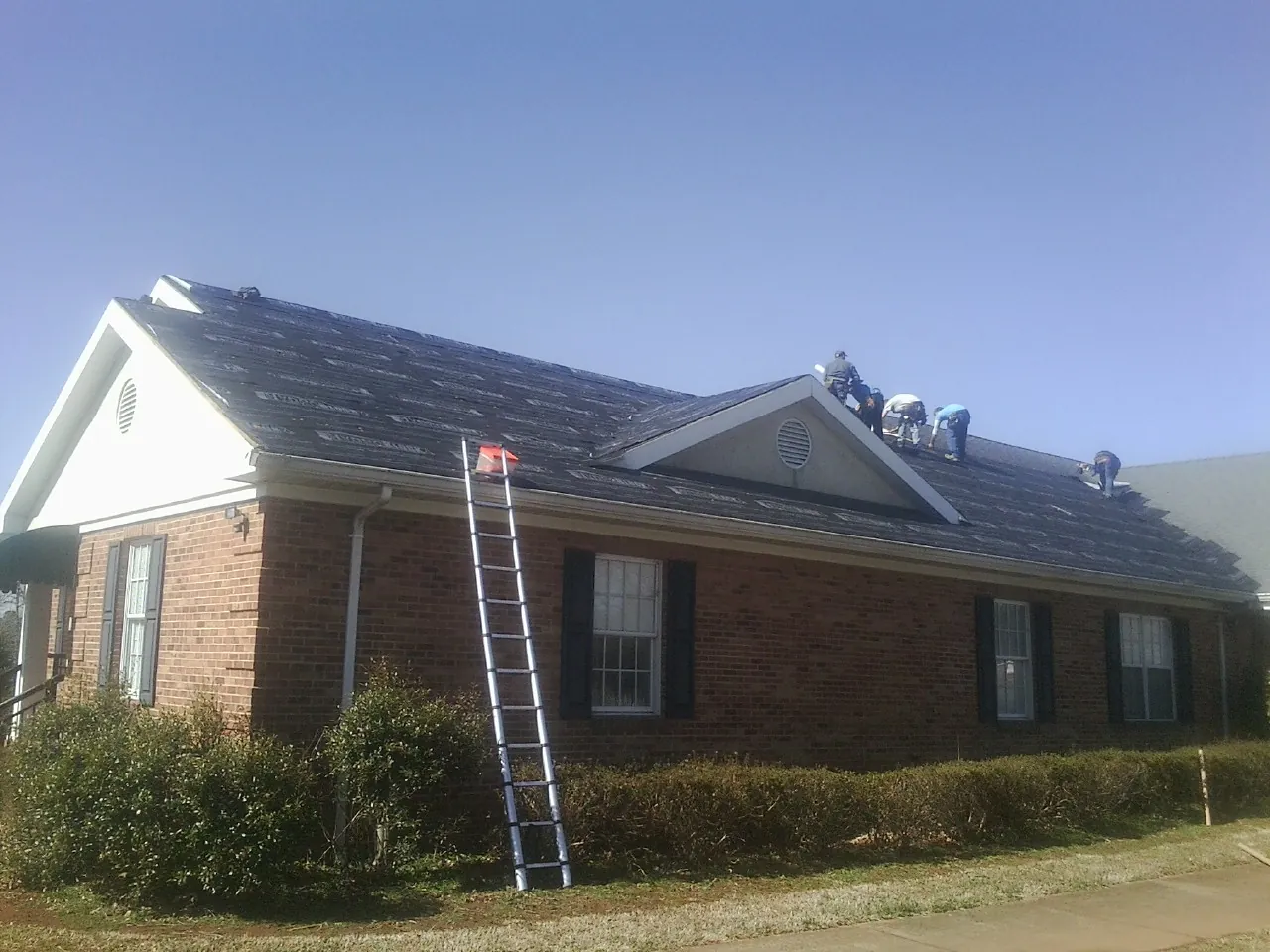 Crew tearing shingles off a brick ranch roof with a ladder set — Metal Roof Repair work by our crew in Randalia