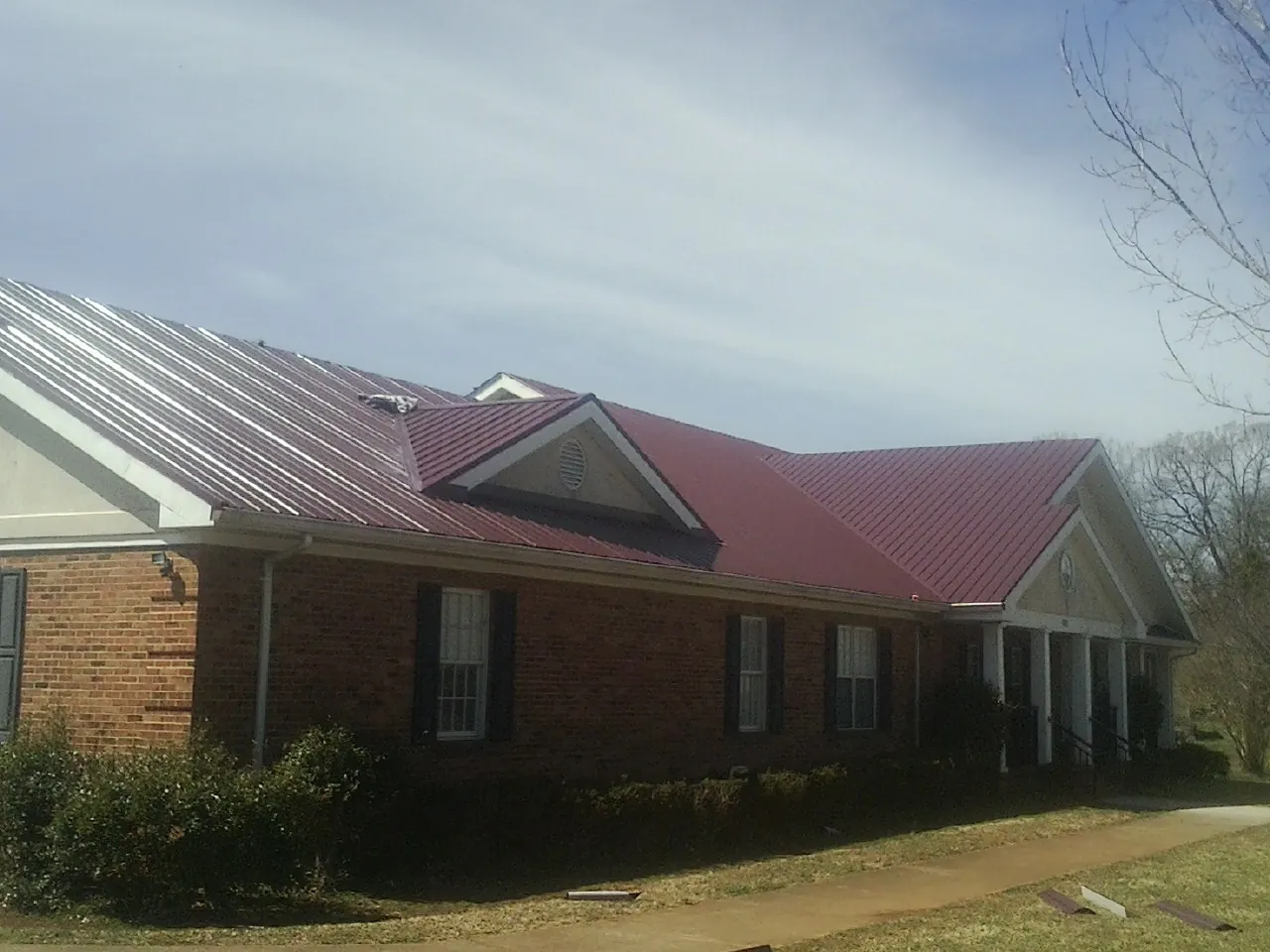 Red metal roof with gabled entries on a long brick building, from a Hail Damage Roof Repair job in Randalia
