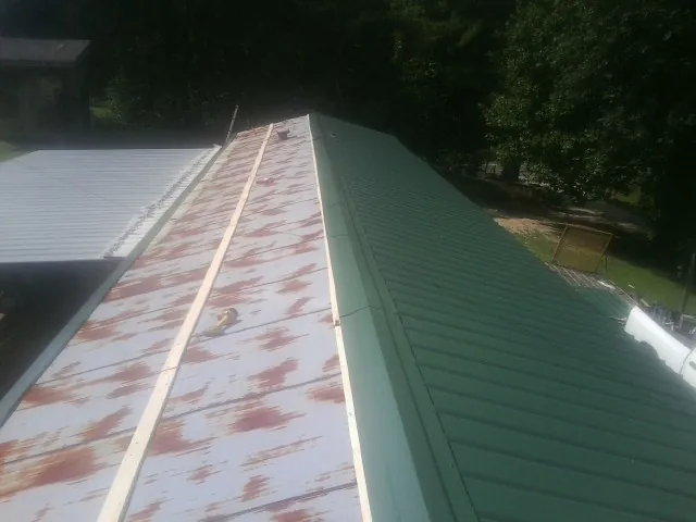 Old rusted panels beside newly installed green metal roofing — Wind Damage Roof Repair by Roofing Brothers in Randalia