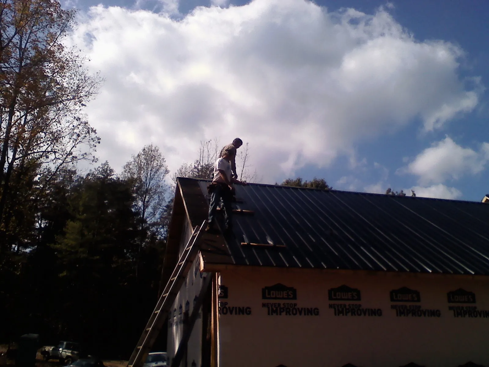 Roofer fastening dark metal panels high against a cloudy sky, from a Roof Inspection job in Randalia