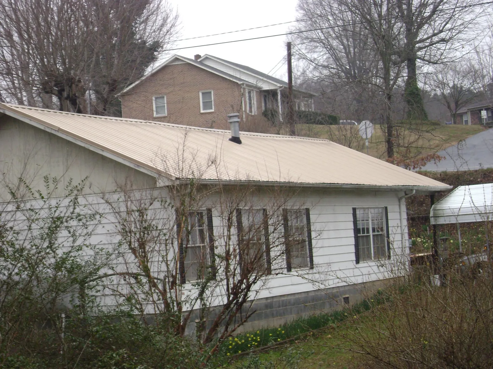 Tan metal roof on a white sided house set into a hillside — Commercial Roofing by Roofing Brothers in Randalia