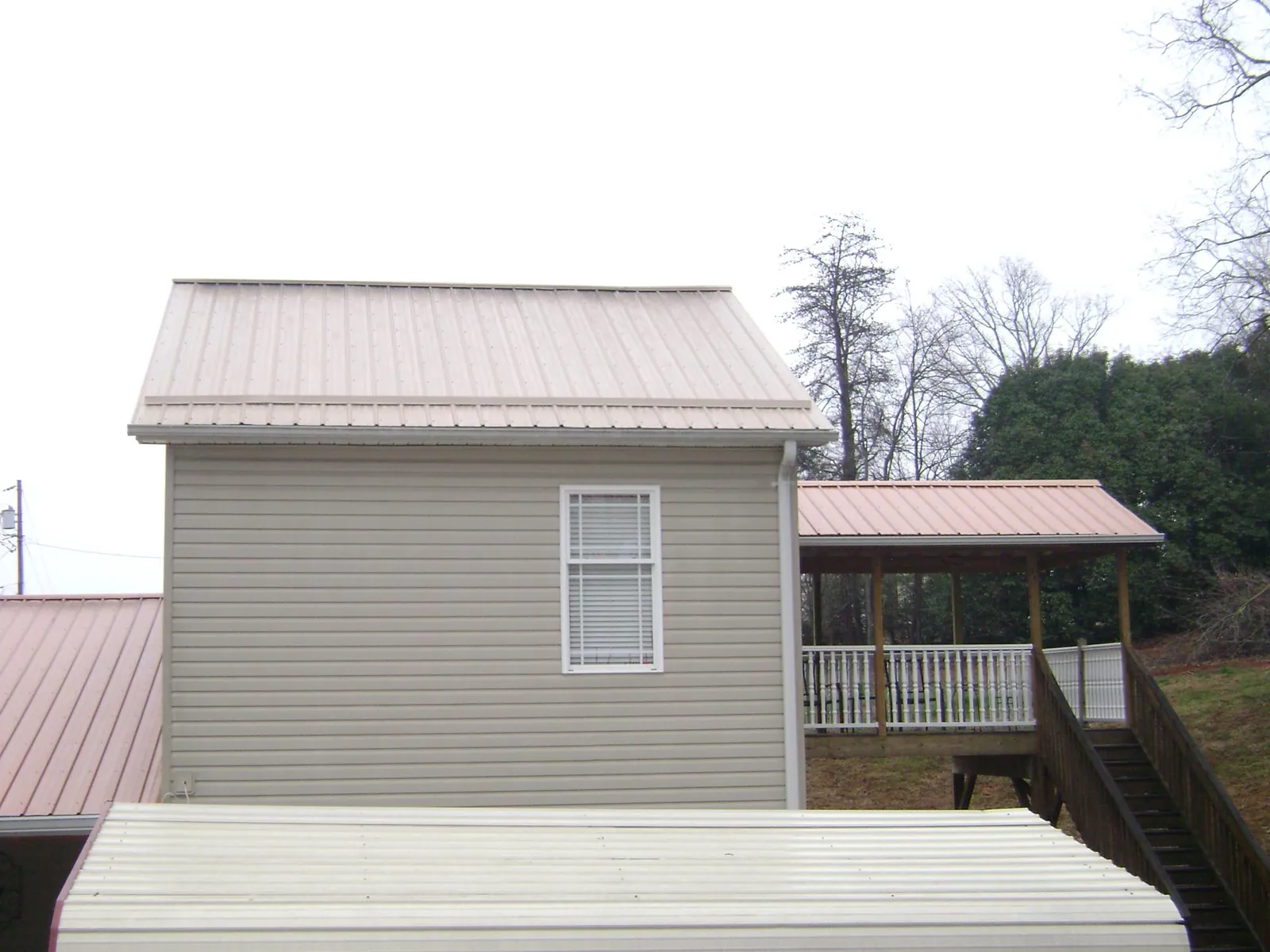 Tan metal roofs on a two story addition and attached porch, from a Roof Replacement job in Randalia
